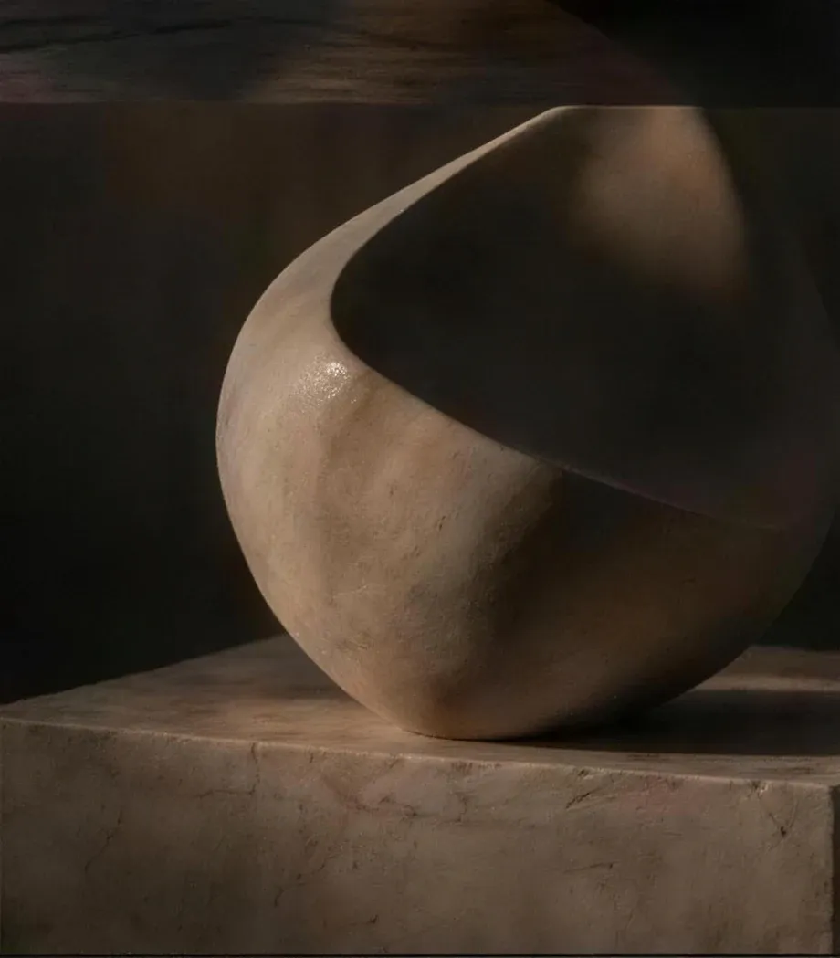 A smooth sculptural form resting on a stone plinth in low warm light