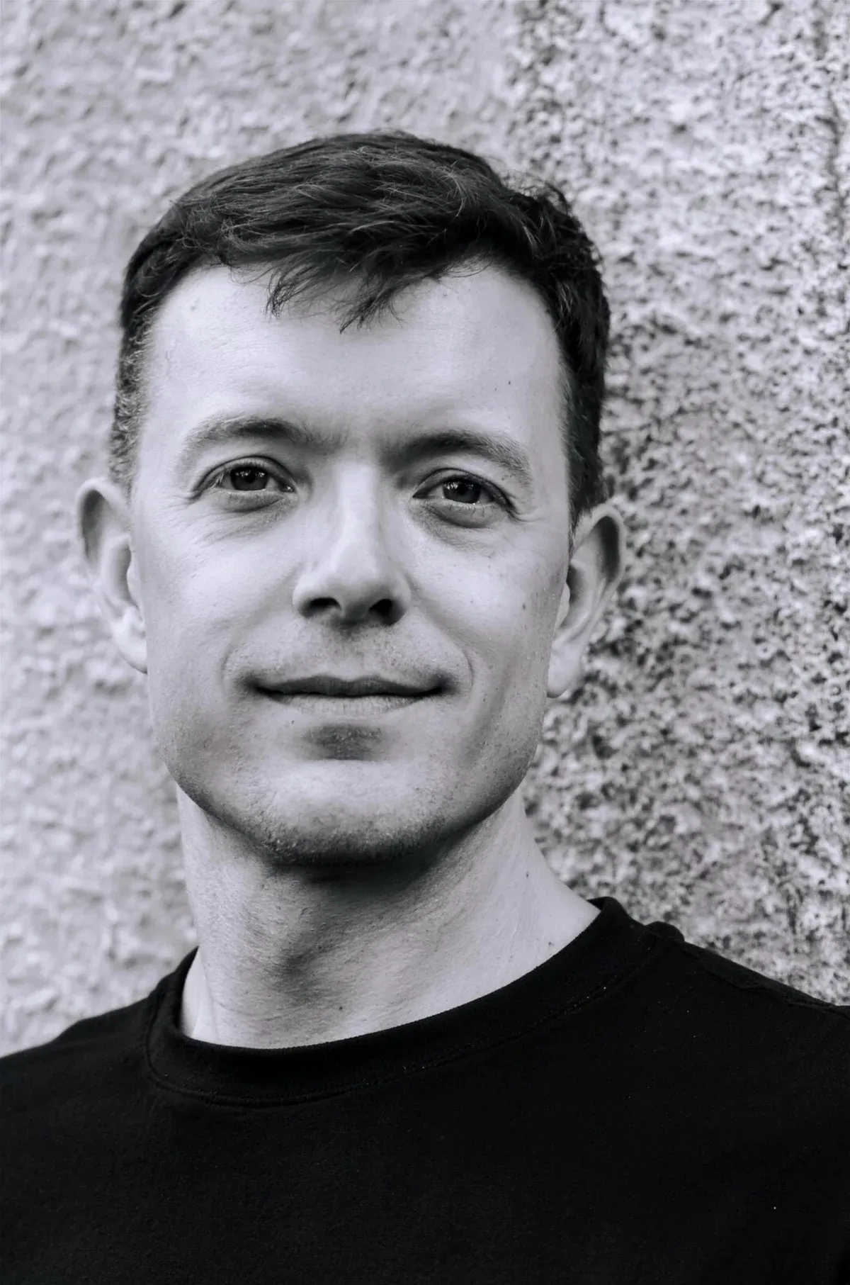 Dr Mikko in a dark shirt, photographed against a textured concrete wall