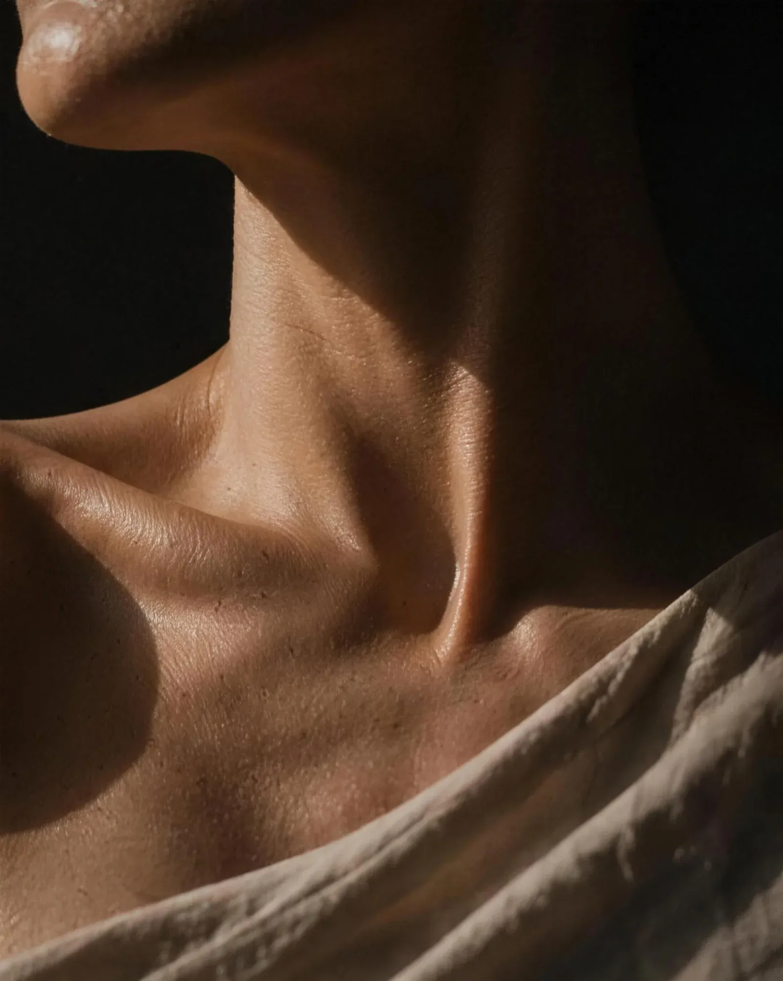 Light falling across the neck and shoulder of a mature person, showing the natural texture and contour of skin