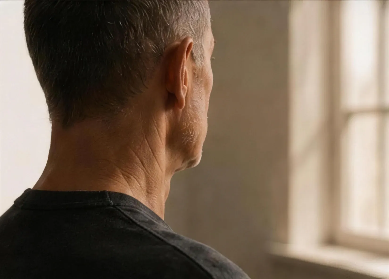 A man seen from behind at the shoulder and neck, lit by soft window light