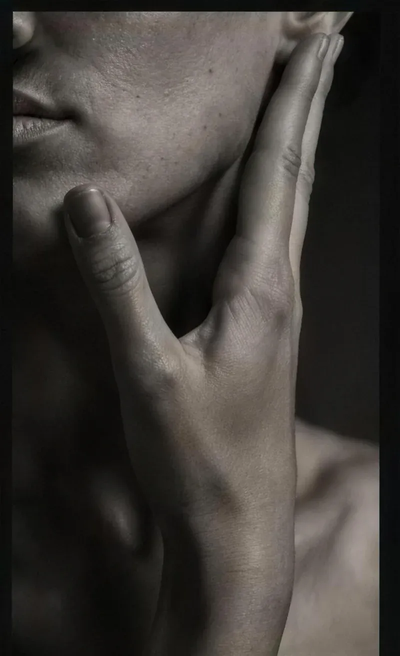 Close crop of a face in profile with a hand resting against the jaw, lit softly from one side