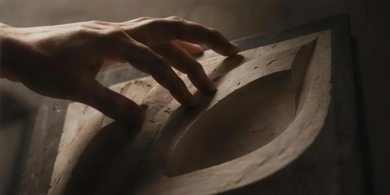 A hand tracing the surface of a carved form in warm directional light